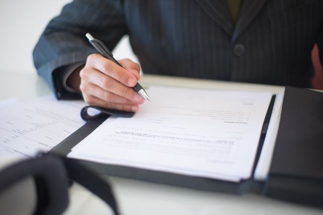person in a suit looking over a document with a pen